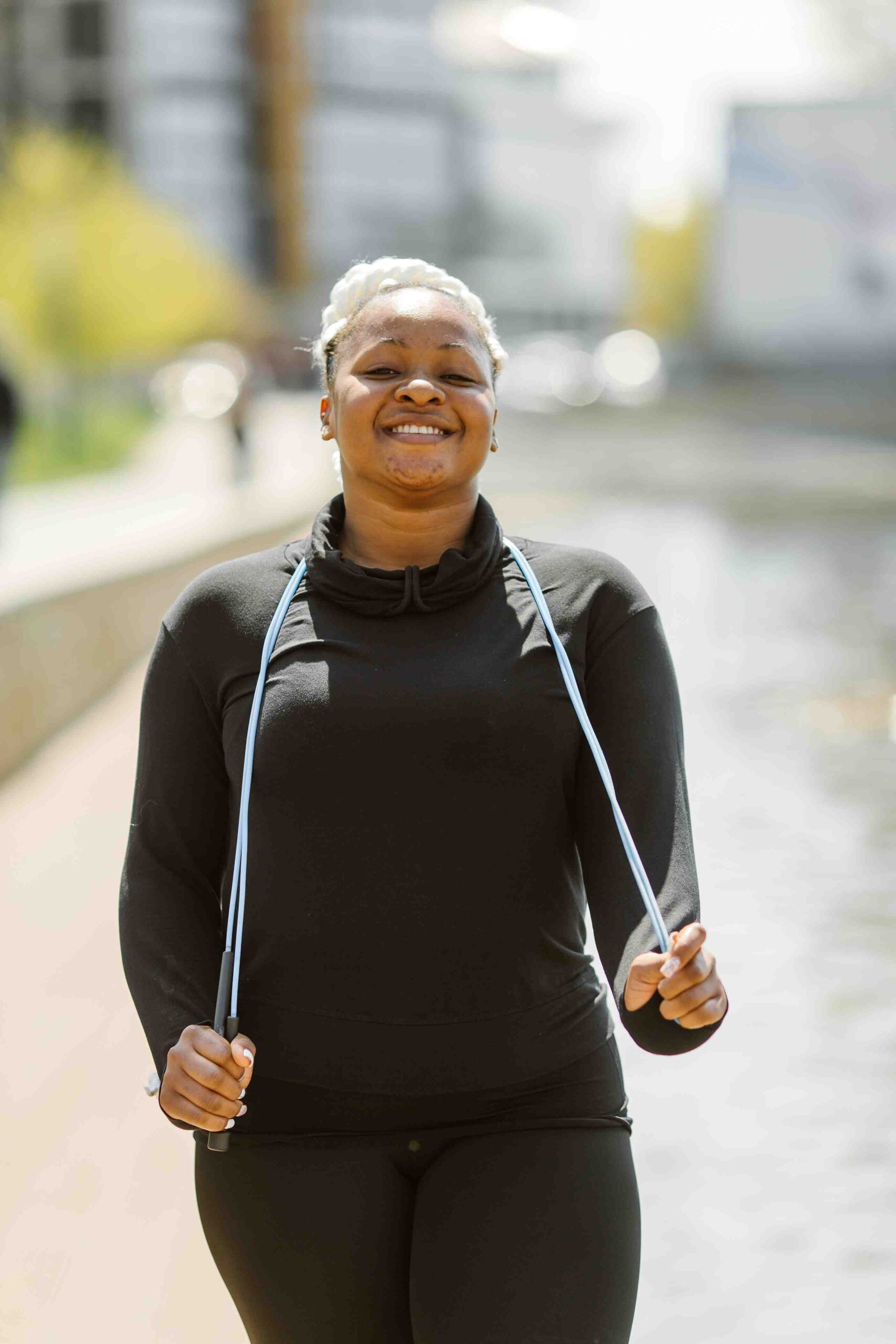 A person grins as they jump rope outdoors, near a tranquil body of water, embracing the energy and joy that comes after outpatient alcohol treatment.