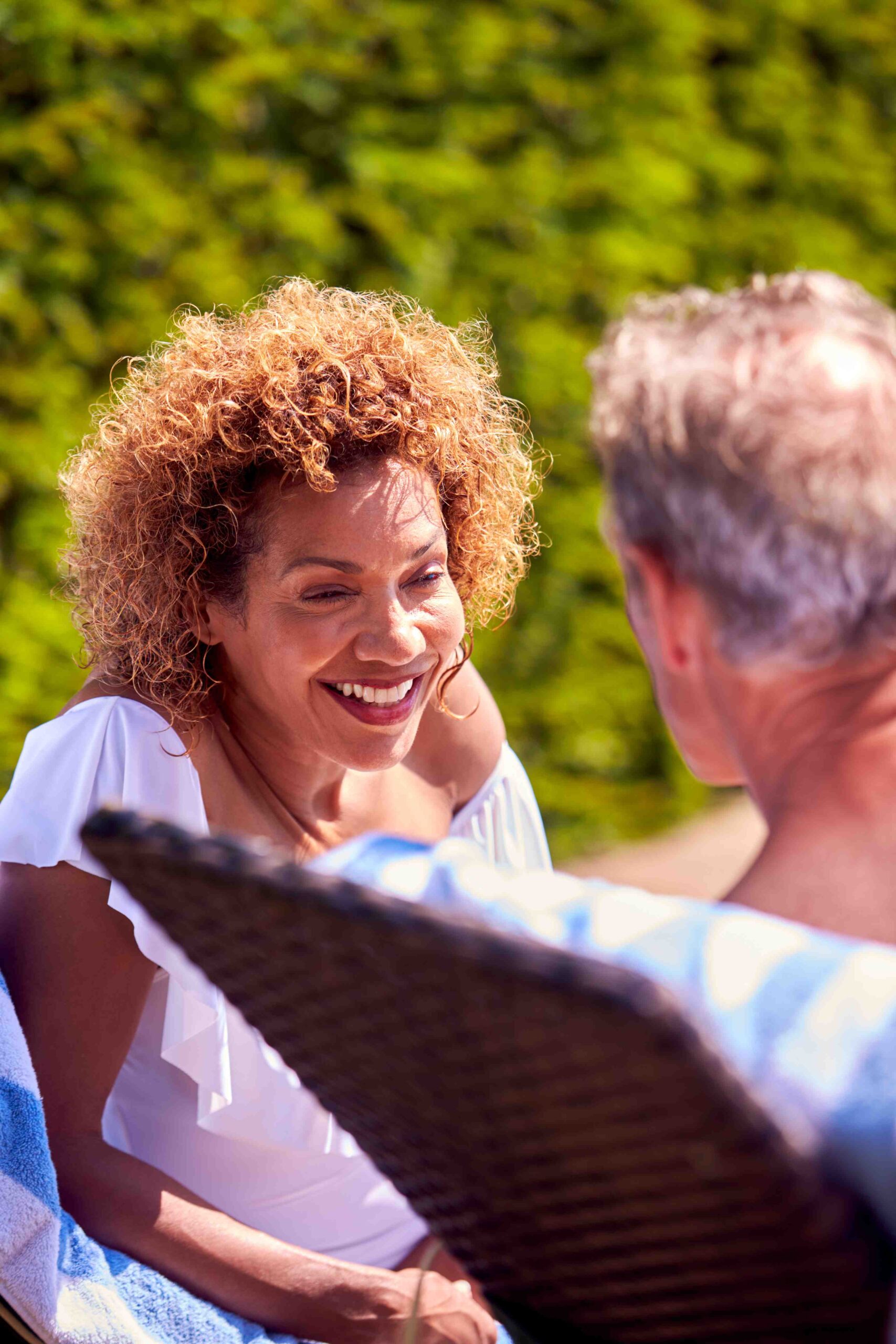 A woman smiles at a man while sitting outside on a sunny day, finding comfort and connection amidst her journey through intensive outpatient treatment.