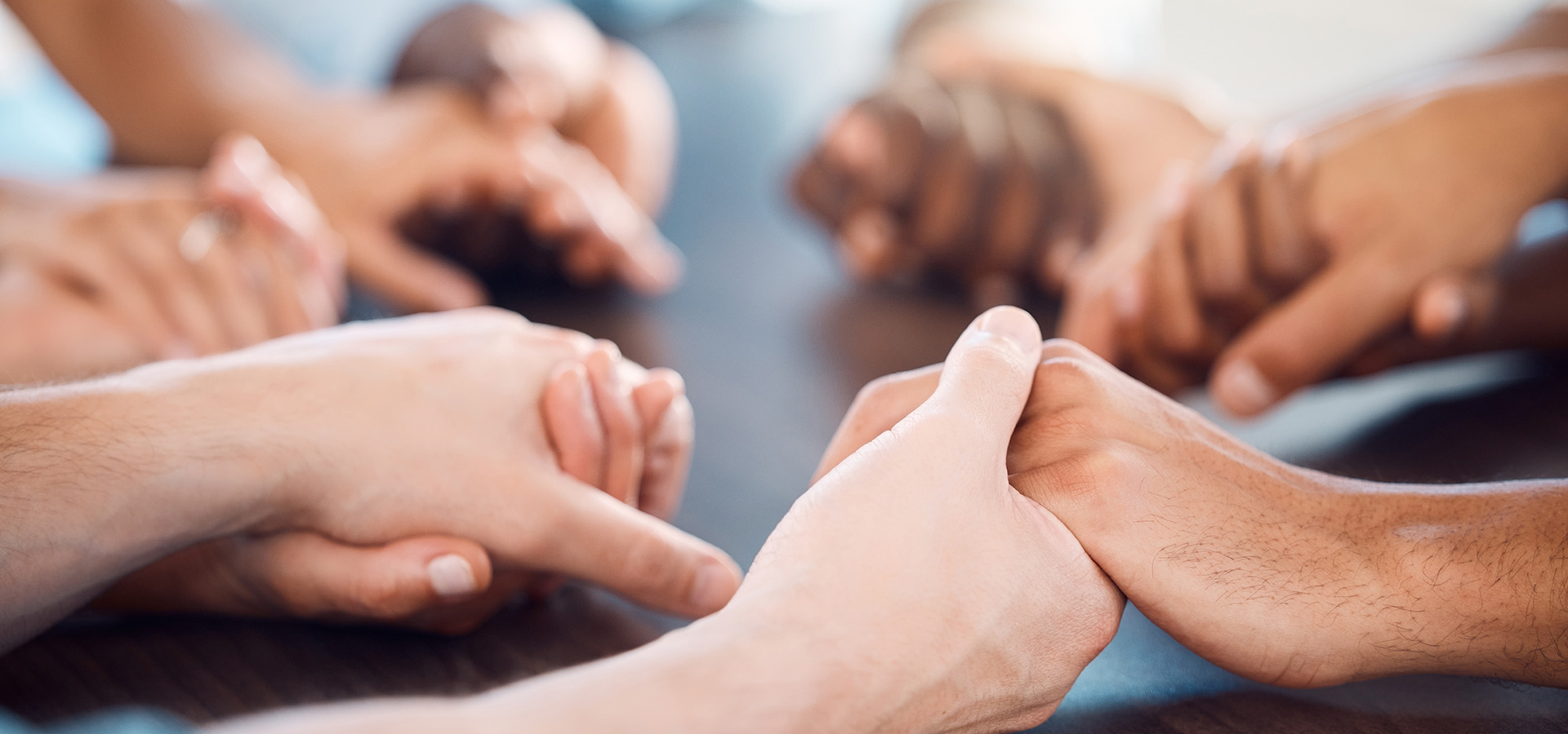 A group of people holding hands around a table in a display of unity and support.